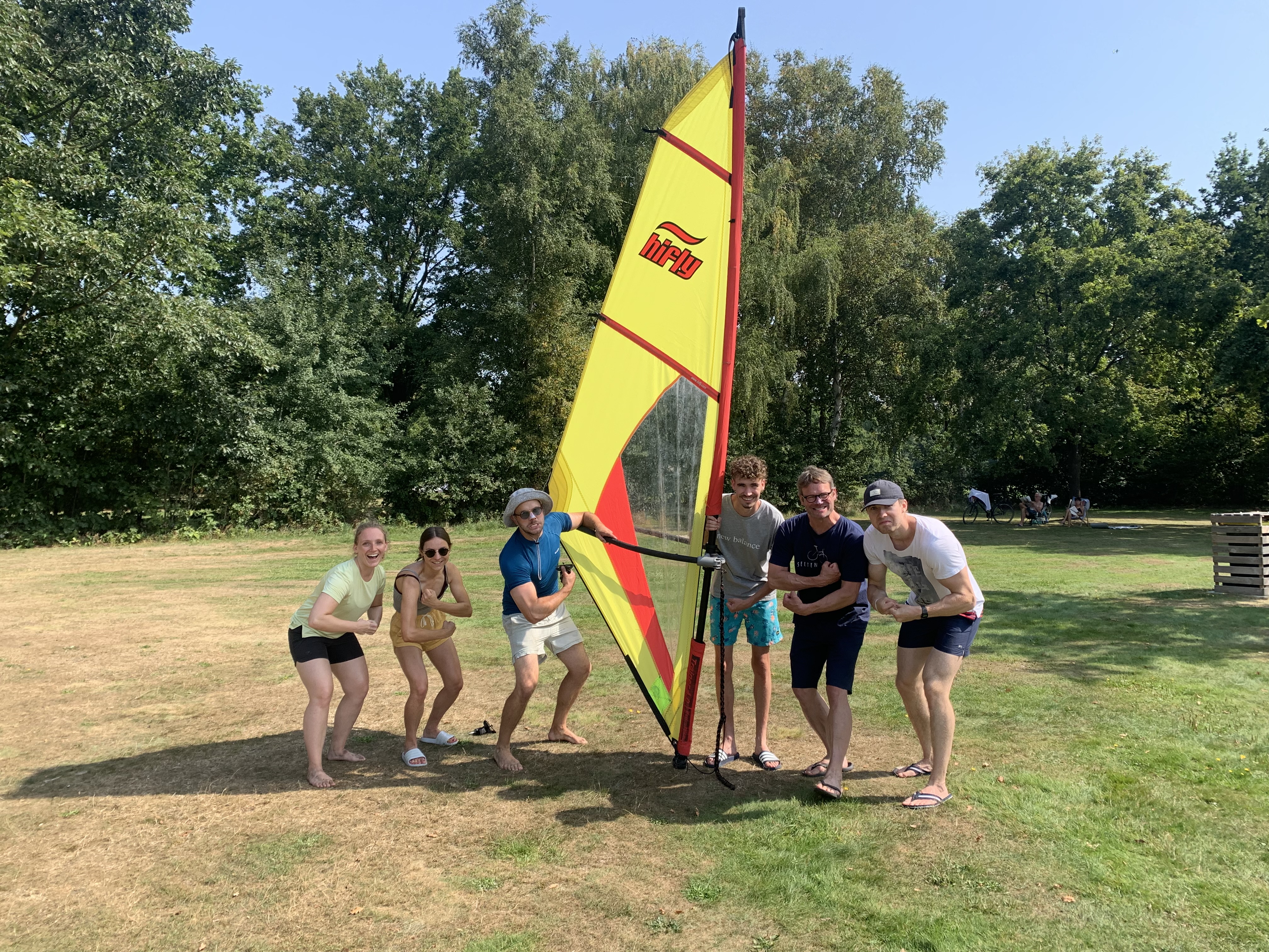 Surfen am Tankumsee - Bild 2: Teilnehmergruppe steht auf einer Wiese und hält ein gelbes Surfsegel aufgerichtet